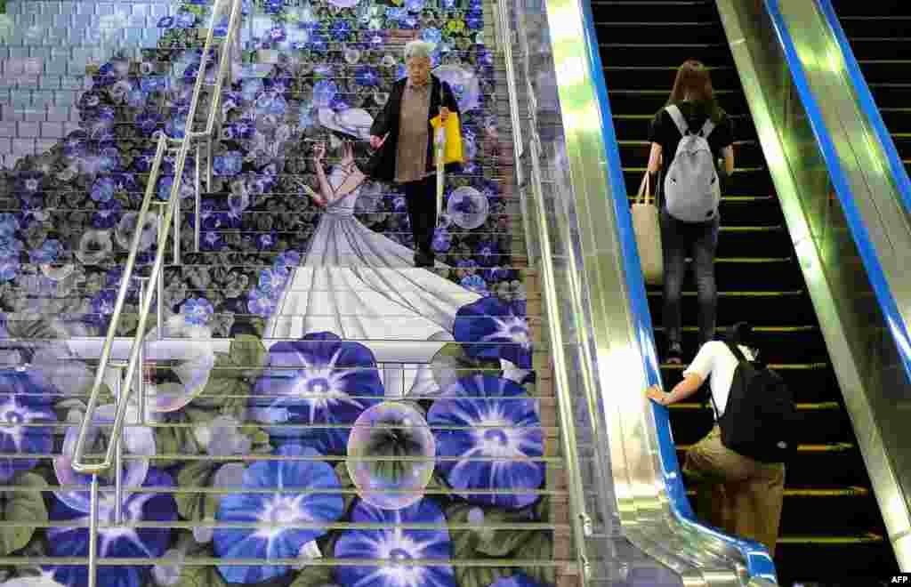 A commuter (L) walks down stairs adorned with artwork of a girl surrounded by morning glories at an entrance of the JR Kumagaya Station in Kumagaya, Saitama Prefecture, Japan.