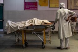 FILE - A man stands next to the body of his wife, who died due to breathing difficulties, inside an emergency ward of a government-run hospital, amidst the coronavirus pandemic, in Bijnor, Uttar Pradesh, India, May 11, 2021.