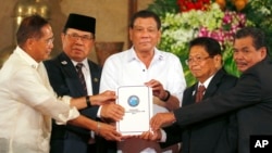 Philippine President Rodrigo Duterte, center, holds the draft of the Bangsamoro Basic Law (BBL) together with, government Peace Panel chief negotiator, Al-Hajj Murad, chair of Moro Islamic Liberation Front Monday, July 17, 2017 in Manila, Philippines.