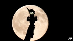 In this July 31, 2015, file photo, a blue moon rises behind the torch of the Statue of Liberty seen from Liberty State Park in Jersey City, N.J. A blue moon happens when the moon rises in its full stage twice during the same month. (AP Photo/Julio Cortez)