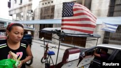 FILE - A woman walks past a bicycle taxi displaying the U.S. and Cuban flags in Havana, Dec. 17, 2014.