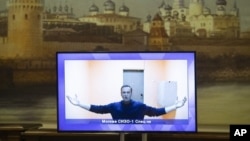 Russian opposition leader Alexei Navalny appears on a TV screen during a live session with the court during a hearing of his appeal in a court in Moscow, Russia, Thursday, Jan. 28, 2021, with an image of the Moscow Kremlin in the background.