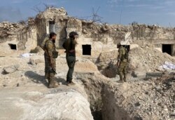 FILE - Turkey-backed Syrian rebel fighters stand near underground tunnels said to be made by the Syrian Democratic Forces (SDF) in Tal Abyad, Syria, Oct. 17, 2019.