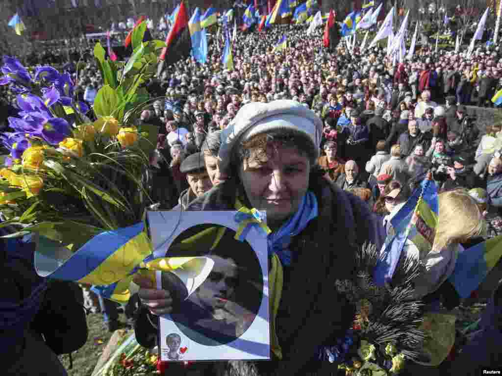 A woman holds a portrait of Ukrainian poet Taras Shevchenko while the crowd solemnly commemorates the 200th anniversary of the birth of its greatest poet&nbsp;takes to mark his 200th birthday near a monument of him in central Kyiv, March 9, 2014.&nbsp; 