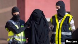 FILE - Masked Spanish police officers lead a detained woman in Melilla, Dec. 16, 2014. Arrest was part of ongoing swoop on suspected efforts to recruit women to go to Syria and Iraq to support Islamic State insurgents.