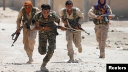 FILE - Kurdish fighters from the People's Protection Units (YPG) run across a street in Raqqa, Syria, July 3, 2017. 