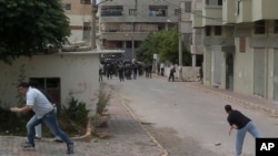 Men throw stones at riot police during clashes in the Mediterranean coastal town of Banias, May 27, 2011.