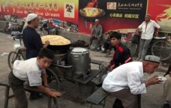 FILE - Uighurs rest near a food stall and Beijing Olympic Games billboards in Kashgar in China's western Xinjiang province, Aug. 6, 2008.