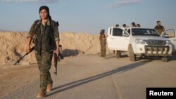 A female member of the Sinjar Resistance Units (YBS), a militia affiliated with the Kurdistan Workers' Party (PKK), carries a sniper and an AK-47 rifle in the village of Umm al-Dhiban, northern Iraq, April 29, 2016.