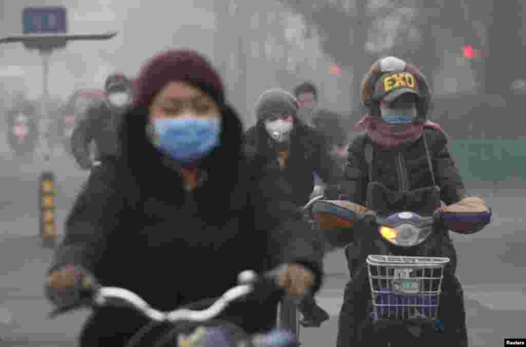 Pessoas usam máscara de protecção enquanto andam de bicicleta, num dia de nível extremo de poluição em Pequim. China, 8 de Dezembro 2015