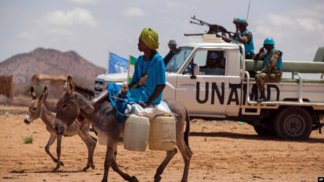 Seorang mengendarai keledai di Khor Abeche, Darfur, Sudan, sementara pasukan perdamaian PBB tampak siaga di belakangnya (foto: dok).