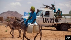 Seorang mengendarai keledai di Khor Abeche, Darfur, Sudan, sementara pasukan perdamaian PBB tampak siaga di belakangnya (foto: dok).