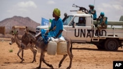 FILE - A man rides his donkey past Tanzanian UNAMID troops standing guard at a camp for internally displaced people (IDP) in Khor Abeche, South Darfur, Sudan. 