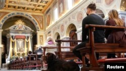 A dog sits next to faithful who attend an Easter Mass in the San Lorenzo in Lucina church, amid the coronavirus disease (COVID-19) lockdown, in Rome, Italy, Apr. 4, 2021. 
