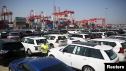 FILE - A worker inspects imported cars at a port in Qingdao, Shandong province, China, May 23, 2018. 