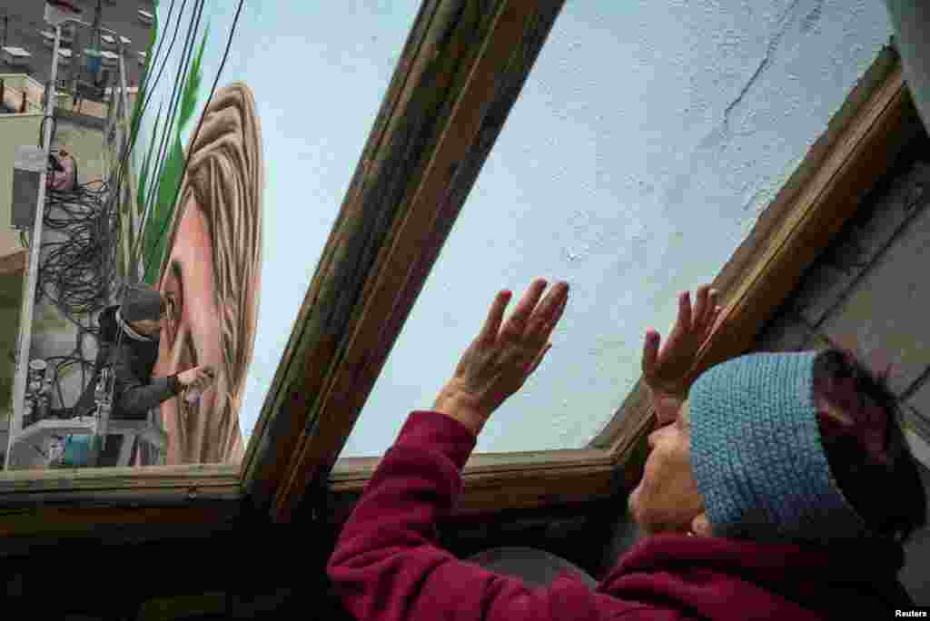 Tamara Bordus observa mientras el artista callejero, Eugene Gladenko, pinta un mural de su nieto, en la fachada de la casa donde solía vivir Maksym, en Kiev, Ucrania, el 18 de octubre de 2024.&nbsp;