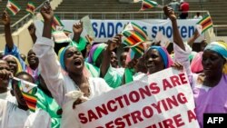 FILE - Demonstrators hold placards as they chant slogans and wave Zimbabwe's national flags during a rally to denounce U.S. and EU economic sanctions, at the National Stadium, in the capital Harare, Oct. 25, 2019. 