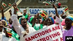 FILE - Demonstrators hold placards as they chant slogans and wave Zimbabwe's national flags during a rally to denounce U.S. and EU economic sanctions, at the National Stadium, in the capital Harare, Oct. 25, 2019. 