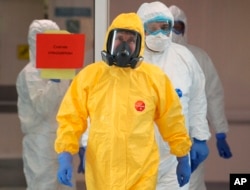 FILE - Russian President Vladimir Putin, center, wearing a protective suit, enters a hall during his visit to the hospital for coronavirus patients in Kommunarka, outside Moscow, Russia, March 24, 2020.