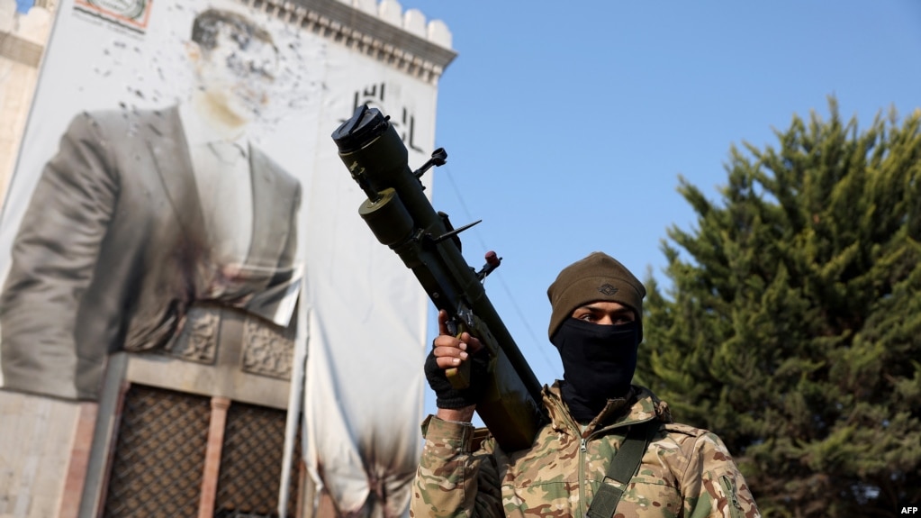 TOPSHOT - An anti-government fighter holds a weapon as he keeps position near a defaced portrait of Syrian President Bashar al-Assad, in the city of Hama after forces captured the central Syrian city, on December 6, 2024.