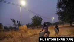 Des cyclistes passent devant un lampadaire alimenté par l'énergie solaire dans le village de Takpapieni, dans la province d'Oti, au nord du Togo, le 14 février 2020. (PIUS UTOMI EKPEI / AFP)