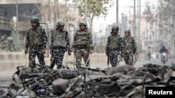 Security forces patrol past charred vehicles in a riot affected area following clashes between people demonstrating for and against a new citizenship law in New Delhi, Feb. 27, 2020.