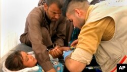 In this frame grab from video, a man comforts his daughter as a doctor treats her after she was taken ill with suspected food poisoning in the Hassan Sham U2 camp for displaced people located about 20 kilometers east of Mosul, Iraq, June 13, 2017.