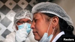 Una trabajadora de la salud le administra un hisopo nasal a una vendedora en un punto de prueba de para detectar COVID-19, en el mercado de Sopocachi en La Paz, Bolivia, el 26 de diciembre de 2020.