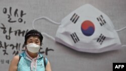 FILE - A woman walks in front of a banner showing a face mask displayed on the wall of the city hall in Seoul, Aug. 20, 2020. 