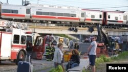 Para penumpang menunggu kendaraan angkutan lain, setela kereta komuter yang mereka naiki kecelakaan di Bridgeport, Connecticut (17/5). Dilaporkan 60 orang cedera dalam musibah tersebut. 