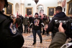 FILE - Trump supporter Douglas Austen Jensen, wearing a QAnon shirt, confronts police on the second floor of the U.S. Capitol after breaching security defenses, in Washington, Jan. 6, 2021.