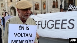 FILE - An elderly man walks with a placard that reads "I was a refugee also," while activists hold up a banner saying "Refugees welcome" during protests against the migration policy of the Orban government in front of the parliament building in Budapest, Sept. 30, 2016.