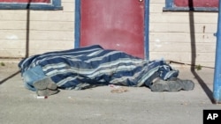 In this Aug. 9, 2013, photo homeless people cover themselves with a blanket on a street in Whiteclay, Neb. Many tribal members live on the tiny town's barren streets to avoid arrest on the nearby reservation for being intoxicated. 