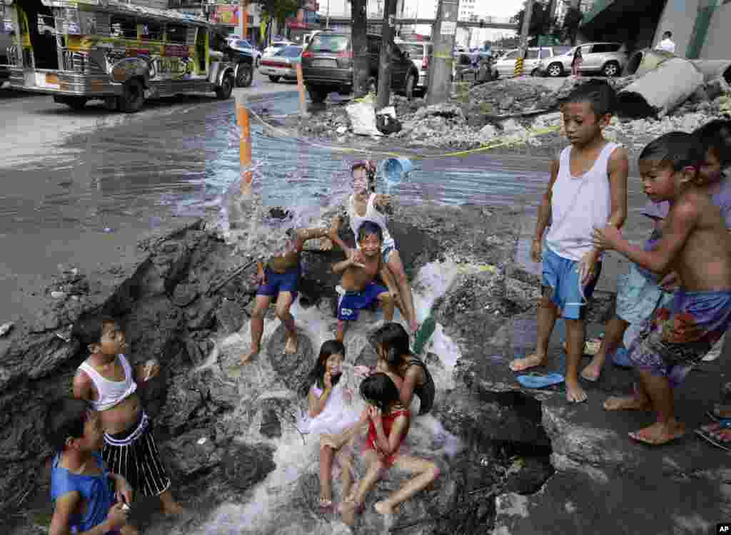 Anak-anak desa mandi dengan memanfaatkan kucuran air dari pipa PAM yang rusak di pinggiran kota Quezon, Filipina.