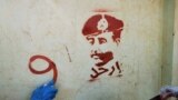 FILE - A person sprays graffiti next to a stencil painting of the Sudan's top army general, Abdel Fattah al-Burhan, with writing in Arabic that reads "leave," during a protest in Khartoum, Nov. 4, 2021, 