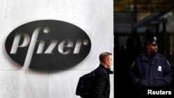 Seorang pria berjalan melewati logo Pfizer di luar kantor pusat Pfizer di New York. (Foto:dok)