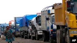 A woman walks next to a queue of truck drivers waiting to fill their diesel tanks in El Alto, Bolivia, Nov. 26, 2024.