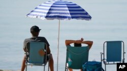 Vacacionistas se relajan bajo una sombrilla en la playa durante una calurosa mañana en Bournemouth, sur de Inglaterra, el 20 de julio de 2021.
