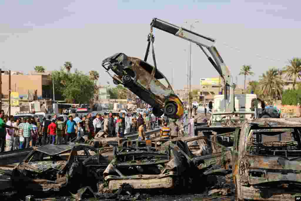 Civiliains and security forces watch as a destroyed car is moved from the site of a car bomb explosion in the southeastern neighborhood of New Baghdad, Iraq, Sept. 10, 2014.