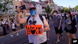 Visitantes caminan por Main Street USA en Disneyland en Anaheim, California, con rótulos que leen "Estamos de Regreso". California, el primer estado de América que puso en marcha un bloqueo por coronavirus, ahora está pasando la página tras la pandemia, e