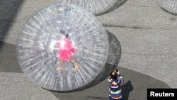 FILE: An artist is seen in a transparent plastic ball during the performance "Tears" by Monster Chetwynd in front of the venue of the Art Basel art fair at the Messeplatz square in Basel, Switzerland September 21, 2021. 