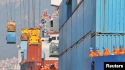 Workers look at cranes lifting containers onto cargo vessels at a port in Yantai, Shandong province, China, Oct. 17, 2019.