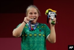 Polina Guryeva of Turkmekistan celebrates on the podium after winning the silver medal in the women's 59kg weightlifting event, at the 2020 Summer Olympics, Tuesday, July 27, 2021, in Tokyo, Japan. She won gold medal and sets a new Olympic record. …