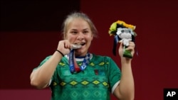 Polina Guryeva of Turkmekistan celebrates on the podium after winning the silver medal in the women's 59kg weightlifting event, at the 2020 Summer Olympics, July 27, 2021, in Tokyo, Japan. 