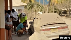 A man fixes a flat tire of a car covered in ash after a series of eruptions from La Soufriere volcano in Orange Hill, Saint Vincent and the Grenadines, April 18, 2021.