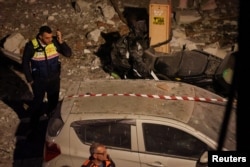 نیروهای امدادی در نزدیکی یک خودروی آسیب‌دیده پس از اصابت موشک جمهوری اسلامی به ساختمانی در مرکز اسرائیل