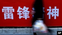 A woman carries her groceries past a Chinese propaganda board depicting "Lei Feng Spirit" on a pavement in Beijing, March 5, 2019. 