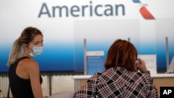 FILE - Travelers wear masks as they wait at the American Airlines ticket counter at O'Hare International Airport in Chicago, June 16, 2020.