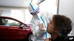 In this March 2, 2021, photo, a German health worker does a COVID-19 test on a French national going to Germany at the German-French border near Saarbrucken.