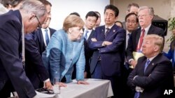 In this photo made available by the German Federal Government, German Chancellor Angela Merkel, center, speaks with U.S. President Donald Trump, seated at right, during the G7 Leaders Summit in La Malbaie, Quebec, Canada, on June 9, 2018.